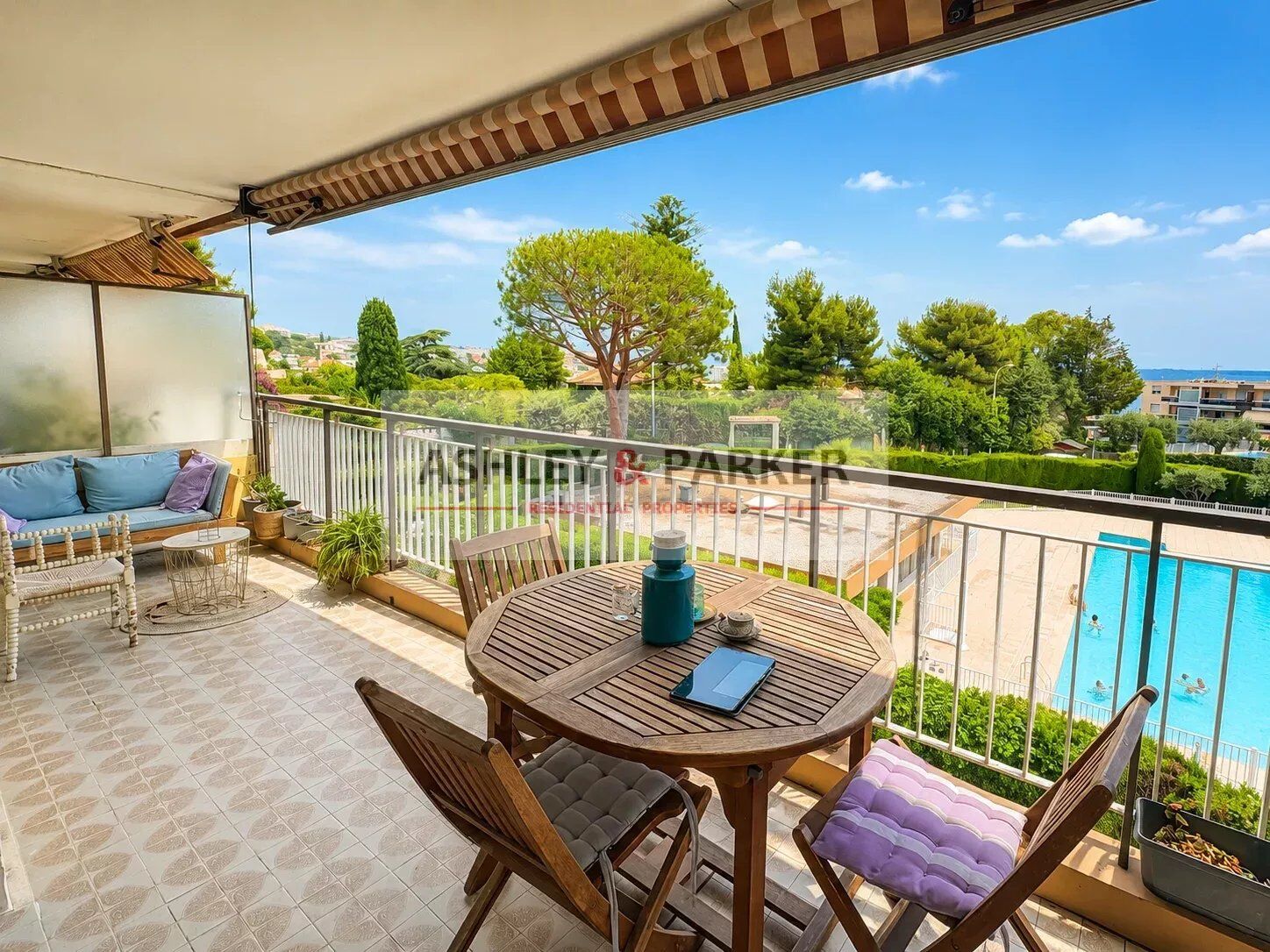 Balcon ensoleillé avec vue sur la piscine et la verdure environnante.